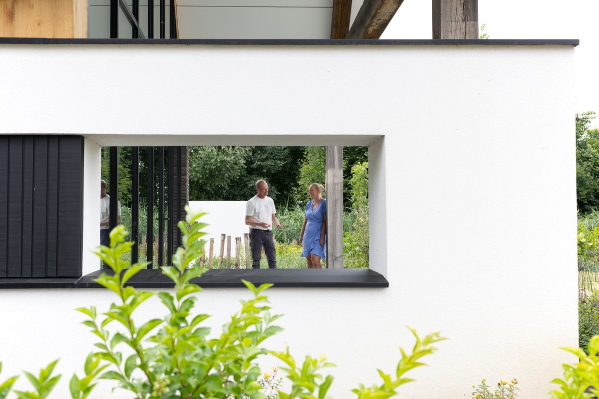Hovenier in gesprek met een klant in de tuin, gezien door een muuropening