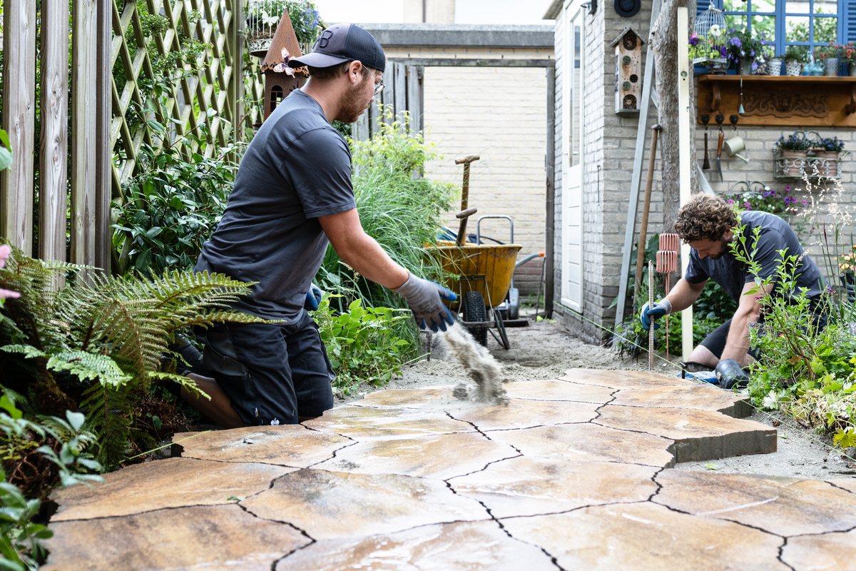 Hoveniers leggen een natuurstenen pad aan tussen de beplanting